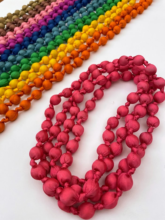 Collana a più giri in seta fucsia a pallini e in sfondo tante collane stesse che formano un arcobaleno